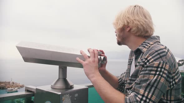 Blonde Man in a Plaid Shirt Looking Through the Telescope From the Observation Deck alt