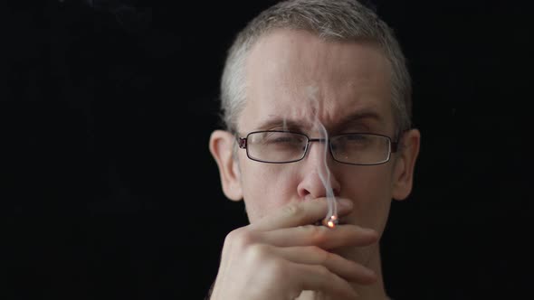 Caucasian Man in Glasses Smokes a Cigarette on a Black Background