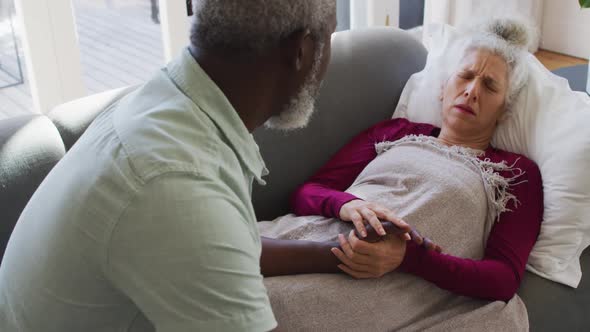 African american man taking care of his sick wife in the living room at home alt