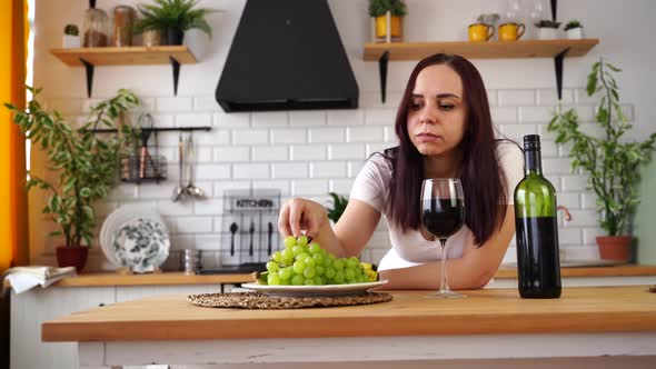Relaxed Young Woman Poses with Glass of Red Wine Standing at Kitchen Table alt