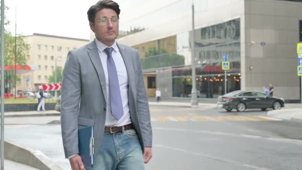 Middle Aged Businessman Walking on Street while Holding a File alt