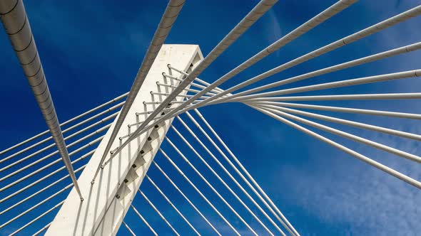 Pylon of a cable stayed bridge under fast moving white clouds in blue sky supported by ropes lines alt