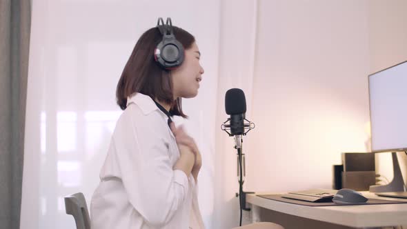 Beautiful Young Asian female influencer talking into a microphone while recording a podcast.