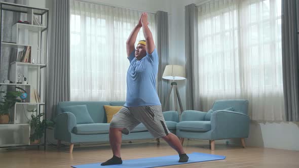Fat Asian Man Doing Yoga In Warrior I Pose On Mat  At Home alt
