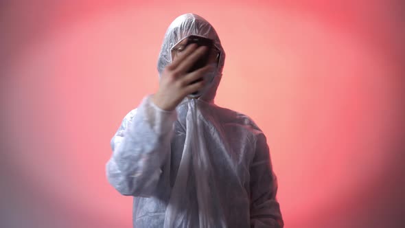 Man in a Protective Suit, Medical Mask and Glasses Takes a Selfie on His Phone on a Red Background