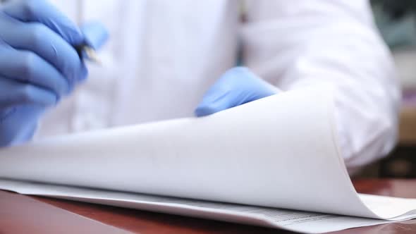 A Doctor In Rubber Gloves Fills Out Documents With A Pen. 