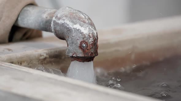 Water flows out of a rusty pipe into a water tank in slow-motion. alt
