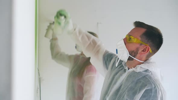 Guy and Girl in Protective Suits Paint Wall with Sprays alt