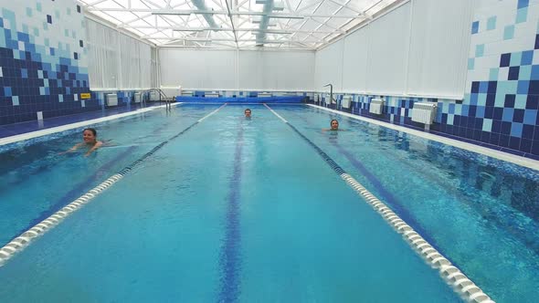 Two Smiling Women and a Young Man Swimming in Different Pool Lanes alt