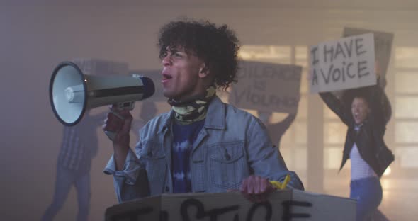 Diverse group of people wearing face masks holding protest signs shouting into megaphone alt