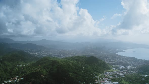 Aerial panoramic view of mountains, dense forest, city, roads, sea, fog and clouds (Saint Lucia) alt