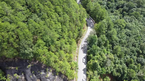 Aerial view of a car running along the mountain road through tropical forest in countryside by drone