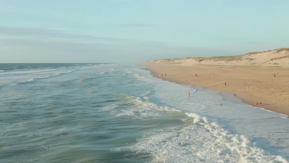 Waves Crashing Onto Shore Line of Beautiful Beach in Afternoon Light with People Having Fun, Aerial alt