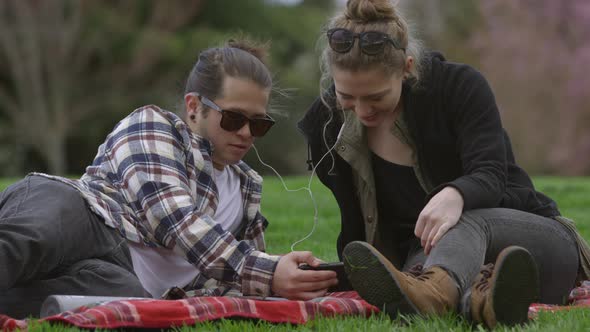Two young people at park on blanket listening to music together