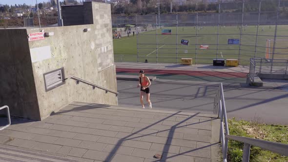 Young woman jogging up stairs in orange sports bra and shorts, Pan Left alt