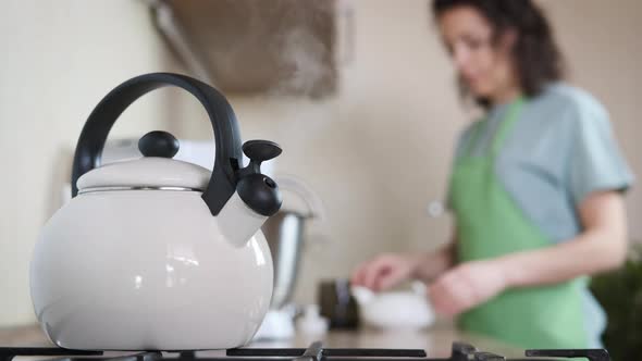 A woman in the kitchen brewing tea. alt