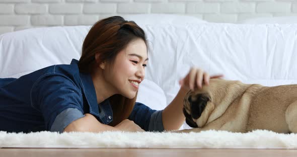 Asian young woman lying and looking face to face and smile with her dog pug breed alt