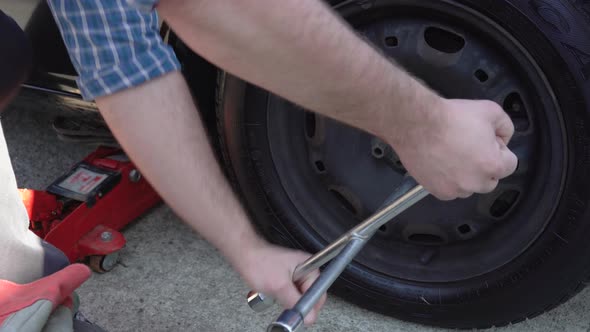 Man Struggling to Unscrew Car Wheel with Winter Tire