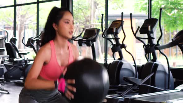 Determined Active Asian Sportswoman Squatting with Medicine Ball During Work Out in Fitness Club alt