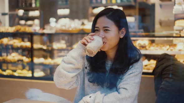 Pretty Young Woman is Drinking Latte Coffee at Cafe Behind the Window