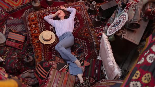 Beautiful happy girl laying on the carpet and rugs in Goreme, Cappadocia, Turkey. Top view drone.	 alt