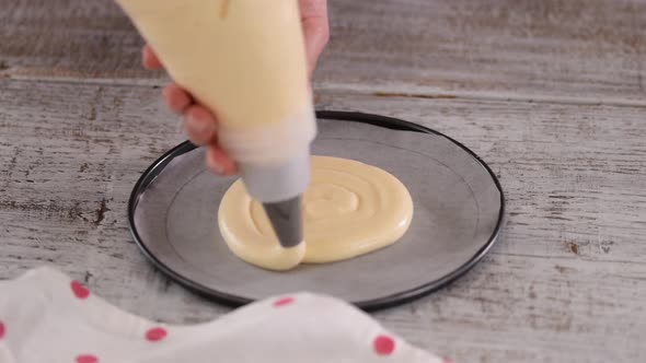 Person with Pastry Bag Piping Cake Batter on Baking Pan at Table