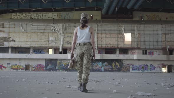 Attractive Young Woman in Military Uniform Walking Slowly in Dusty Dirty Abandoned Building Carrying alt