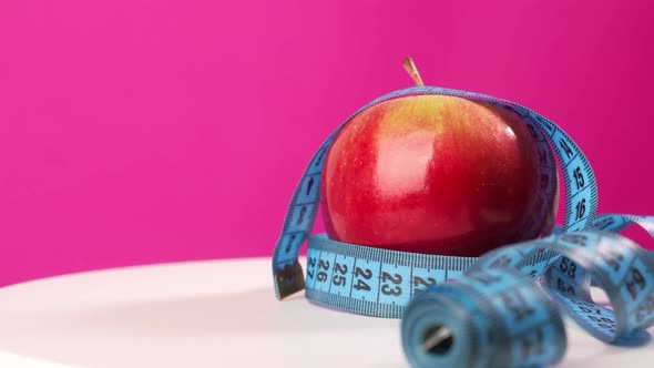 An Apple on a Pink Background is Wrapped in a Centimeter Tape
