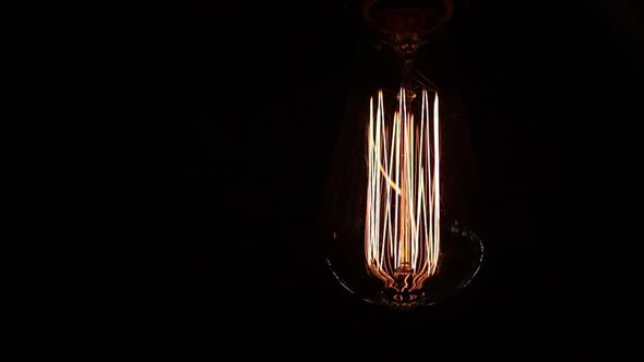 close up of retro light bulb on black background. Tungsten filaments glow with a warm orange light. 