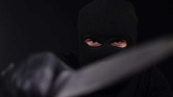 A criminal in a mask with a knife, a crazy maniac, touching his face with a knife in masks alt