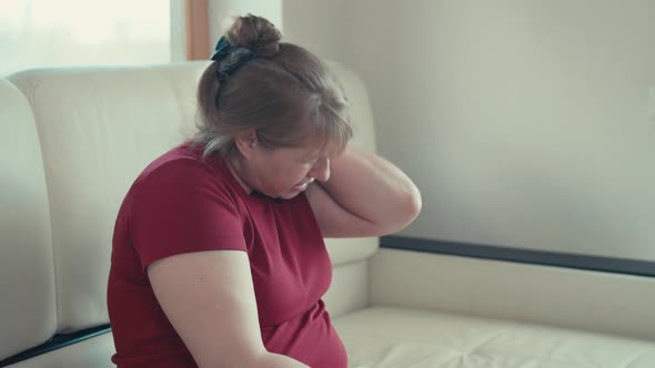 Unhappy tired senior woman rubbing neck feeling pain sit on couch at home alt