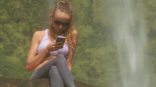 Nice Girl in Sunglasses Reads Sms Near Waterfall alt