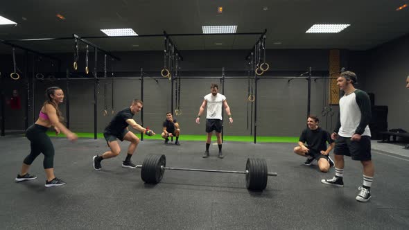 Athletes cheering man while lifting barbell at gym