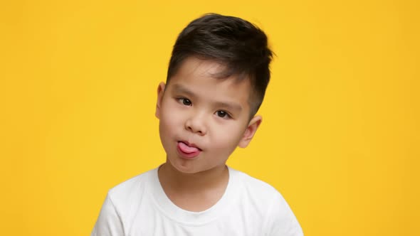 Little Japanese Boy Sticking Out Tongue Posing On Yellow Background alt