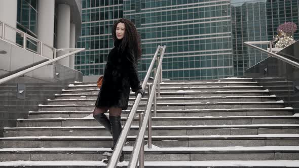 A Curlyhaired Stylish Middleaged Brunette Woman in a Black Fur Coat Walks Alone in the City on a alt