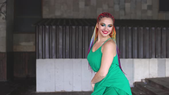 A Girl with Makeup and Multicolored African Braids in a Green Dress Smiles Cutely Walking Along the alt