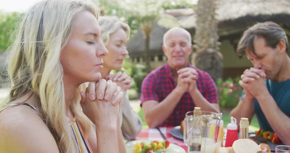 Happy caucasian family having dinner and praying in garden alt