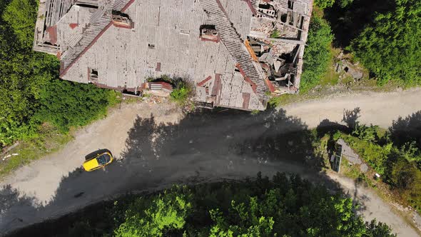 Drone View of an Old Abandoned Highrise Building Past Which a Yellow Car Passes alt