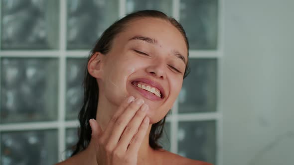 Happy Woman Caring For Face Applying Cream Moisturizer In Bathroom alt