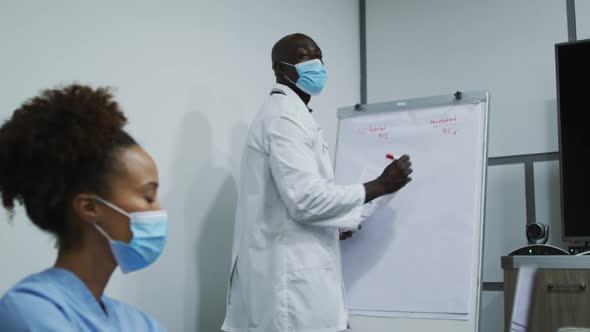 African american male doctor in face mask giving presentation to mixed race female doctor in office alt