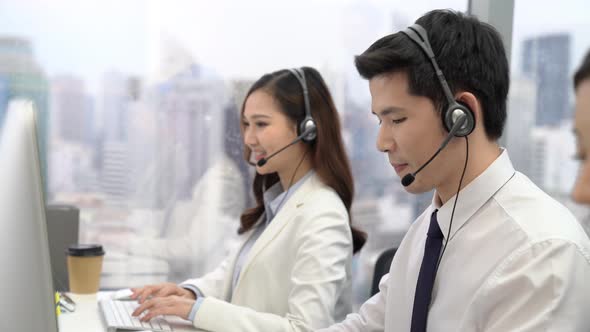 Group of Asian call center telemarketing agents talking on their headsets at office in the city