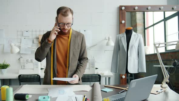 Clothes Designer Discussing Sketches of New Collection Talking on Mobile Phone and Using Laptop in alt