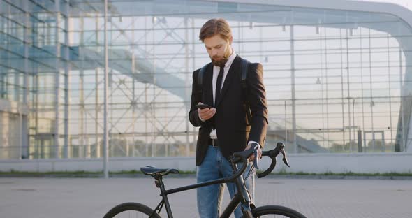 Office Manager Standing in front of Big Glass Building and Typing Message to Somebody on Phone alt
