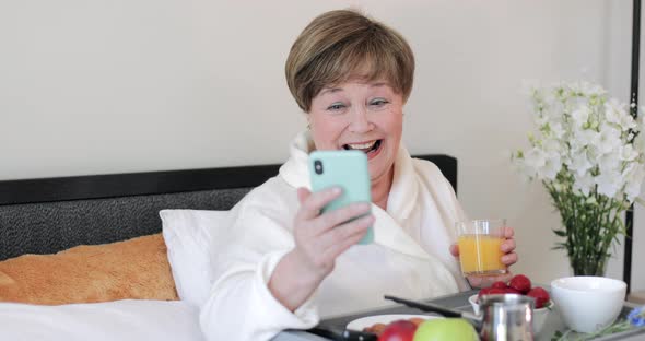 Cheerful Old Lady Looking at Her Modern Smartphone Screen and Laughing. Elderly Woman in Good Mood alt
