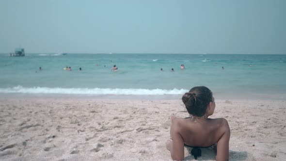 Brunette in Black Bikini with Open Shoulders Lies on Beach alt