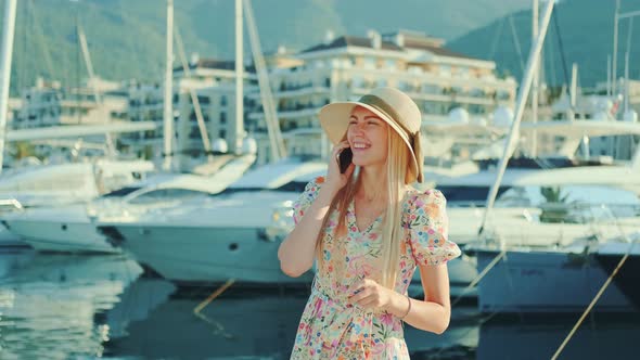 Elegant Woman Speaking on Smartphone on the Street with Yachts in the Background