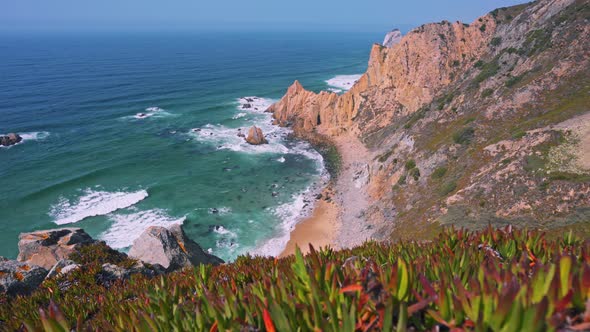 Footage of Praia Do Ursa Beach with Beautiful Orange Colored Cliffs and Foliage in Foreground alt