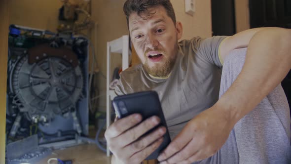 A Man Fixes a Washing Machine and Watches Instructions on His Phone