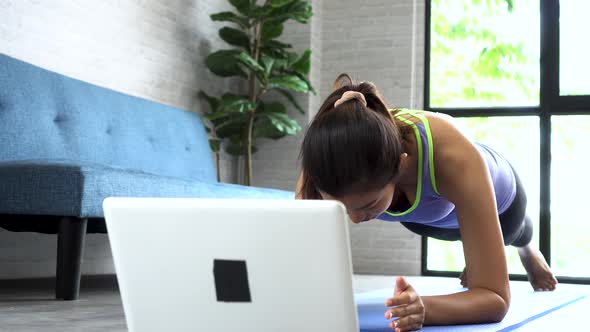 Asian Woman in Sportswear Doing Plank Poses While Watching Fitness Training Class on Computer Online alt