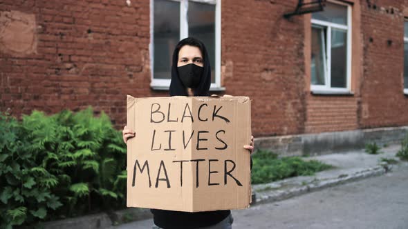 Man in Mask Stands with Cardboard Poster in Hands  BLACK LIVES MATTER